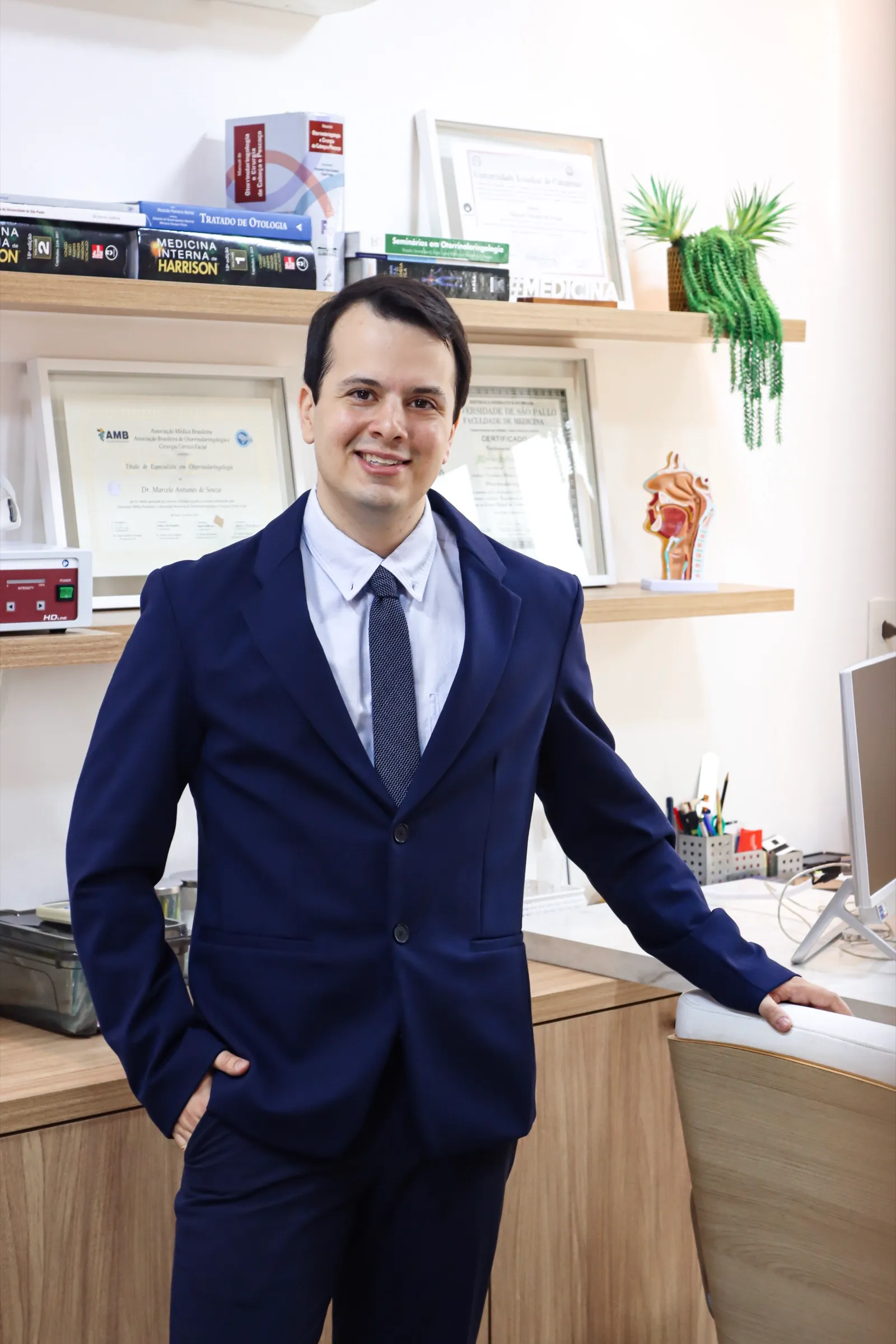 Dr. Marcelo Antunes de Souza no consultório, com diplomas ao fundo